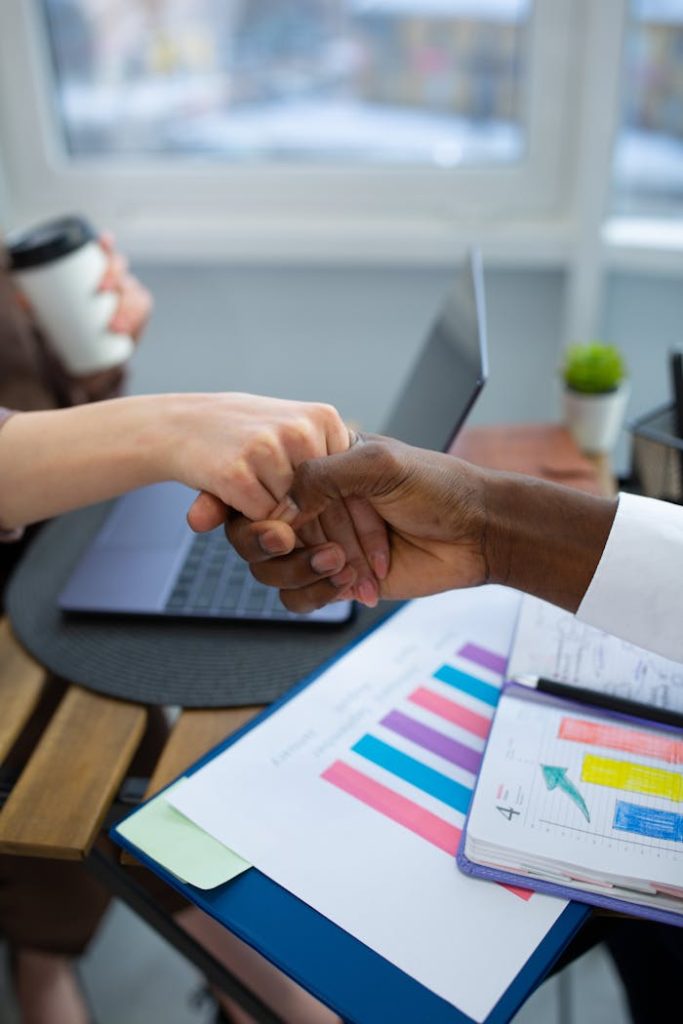 pexels-photo-6931022 Two business professionals fist bump over a work desk with reports and a laptop.